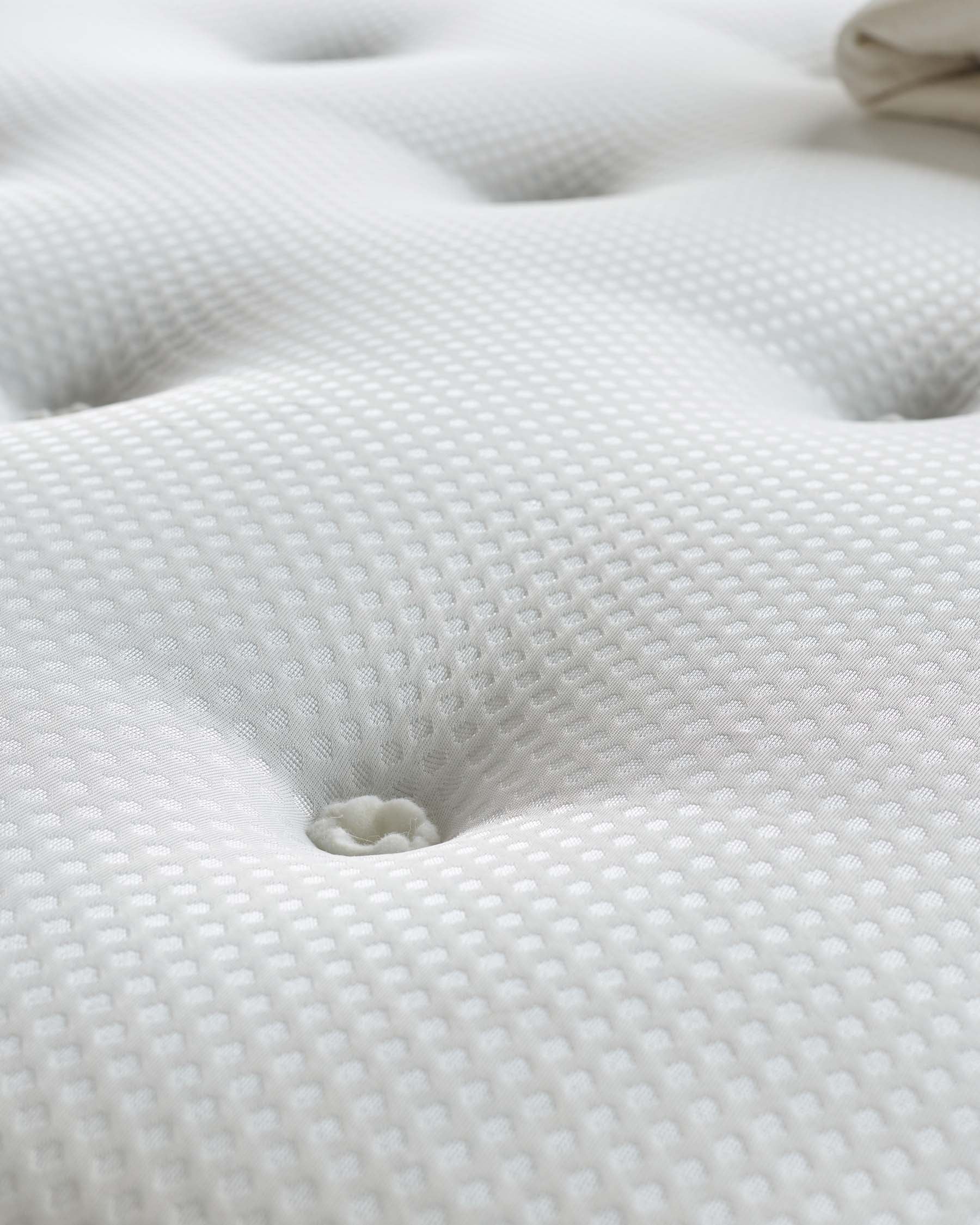 Close-up texture of a white textured fabric, possibly from a piece of furniture such as a mattress or upholstered item, displaying a detailed waffle weave pattern with a focus on a button tufted detail creating a dimple effect.