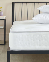 Contemporary metal frame bed with a minimalist headboard design consisting of horizontal bars, paired with a thick, white patterned mattress. On the nightstand to the left, a small vase with a single flower complements the scene.