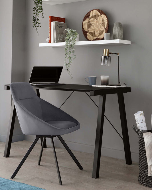 Modern minimalist home office setup with a sleek black writing desk featuring an A-frame leg design and a contemporary upholstered chair in charcoal grey with a curved backrest and angled wooden legs. A floating white shelf is mounted above the desk, not part of the furniture for sale.