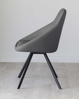 Modern minimalist chair with a sleek grey upholstery and angled black metal legs, against a white wall on a light wooden floor.