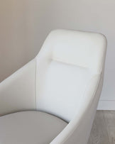 Modern white leather armchair with a curved backrest and an ergonomic seat design, featuring visible stitch detailing.