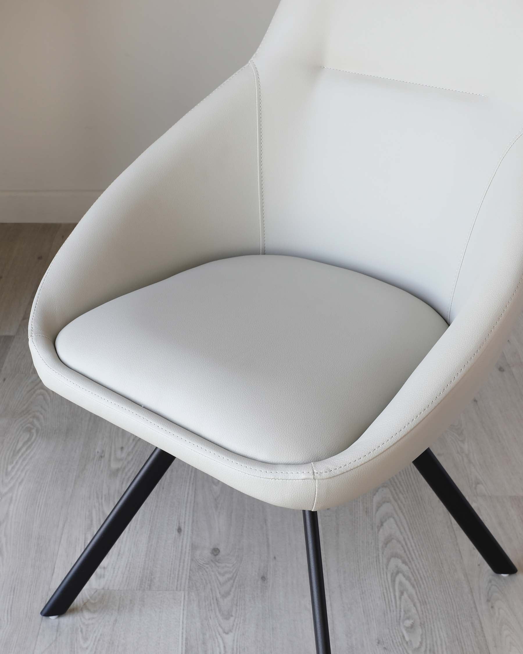 Modern white upholstered armchair with a curved backrest and angled black metal legs, displayed on a light wooden floor.