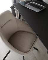 A modern office with a sleek black desk accompanied by a taupe upholstered chair featuring a rounded backrest and angled black metal legs. A laptop, a white mug, and woven basket with a white throw blanket are also arranged on the desk.