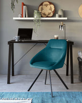 A contemporary black work desk with a minimalist design and diagonal support beams sits parallel to a sleek teal upholstered chair featuring a curved backrest and slender metal legs, contributing to a modern and stylish home office atmosphere.