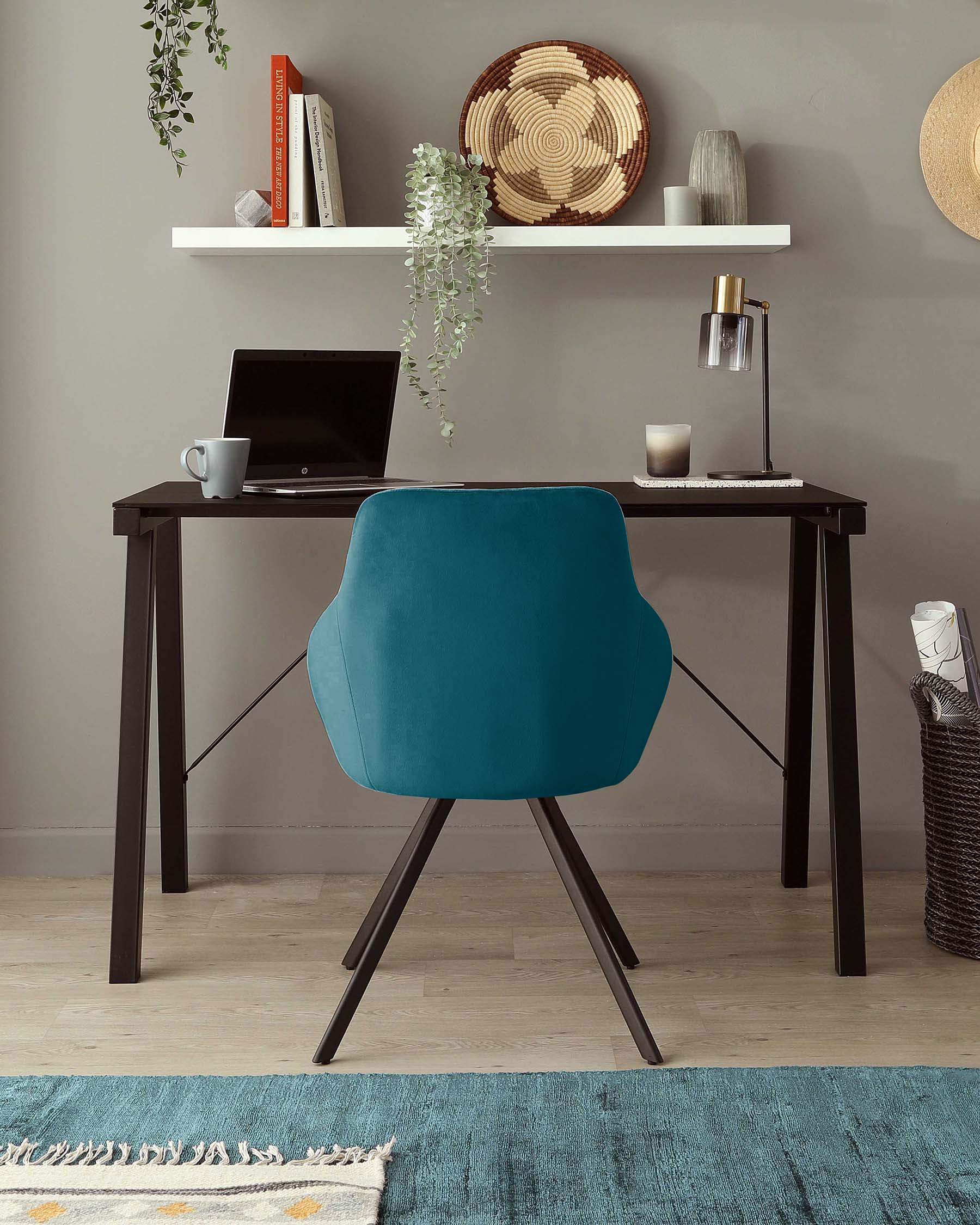 Modern home office setup featuring a sleek black writing desk with straight legs, accompanied by a contemporary teal blue chair with a unique rounded back and angular wooden legs. The desk is accessorized minimally with a laptop, cup, and stylish lamp, and a white floating shelf above displays decorative items, suggesting a clean and fashionable workspace aesthetic.