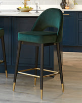 Elegant teal velvet bar stool with a curved backrest and cushioned seat, mounted on a sleek black frame with metallic gold footrest and accents.