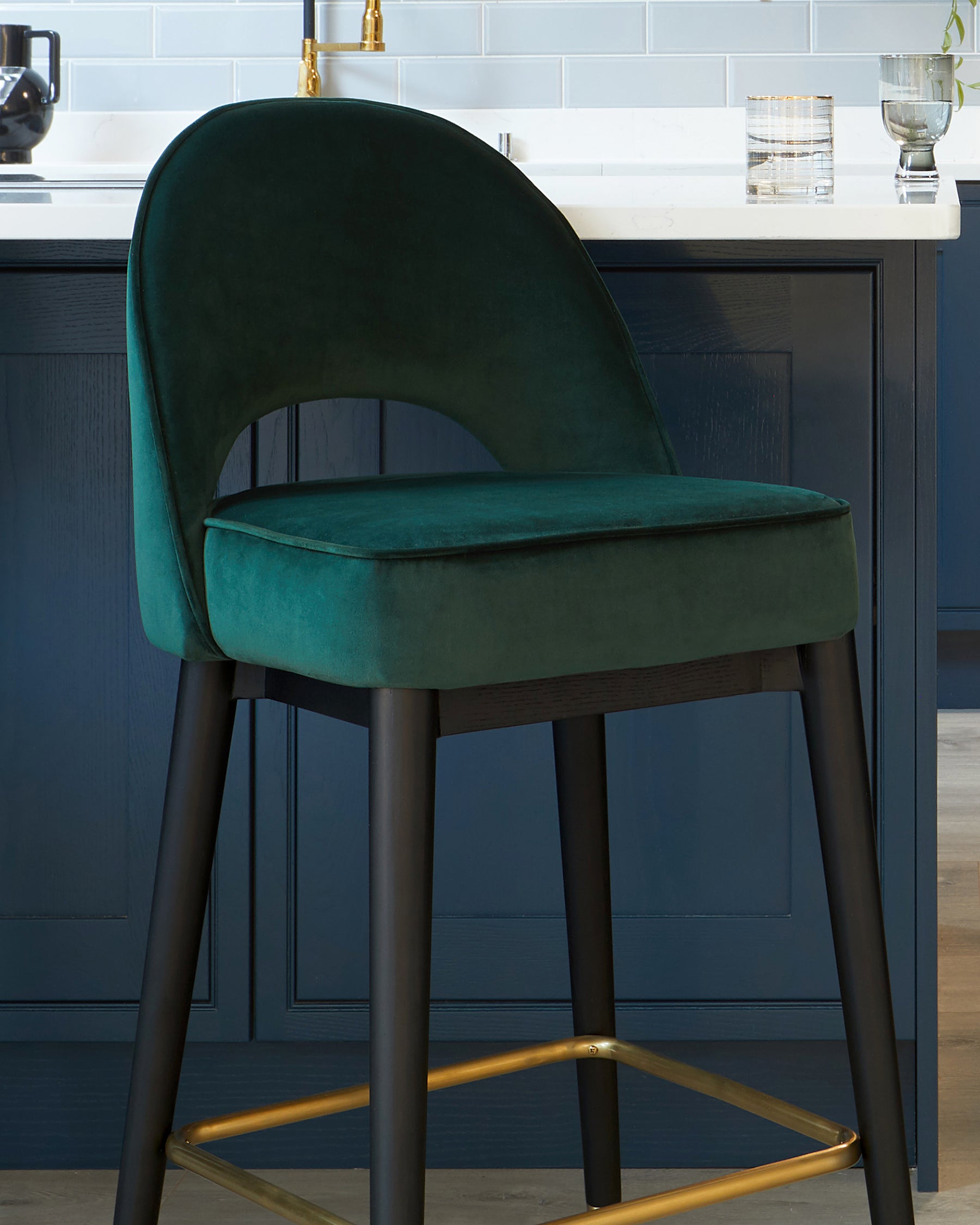 Elegant modern bar stool with plush forest green velvet upholstery and a curved backrest design, featuring matte black legs and golden metal footrest accents.