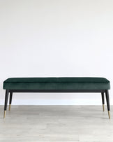 Elegant modern bench with plush dark green velvet upholstery and sleek black frame with gold-capped legs.