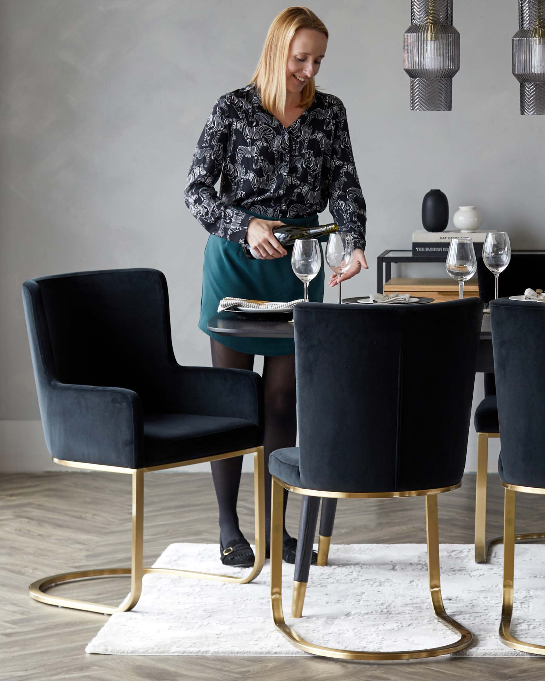 Elegant dining set featuring two plush velvet navy blue chairs with sophisticated gold metal legs and a round matching table with a sleek black top and golden base. The luxurious design exudes contemporary style and comfort.