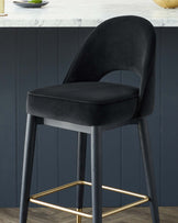 Elegant modern bar stool with a curvaceous black velvet upholstered seat and backrest, featuring sleek black legs with gold-finished footrests.