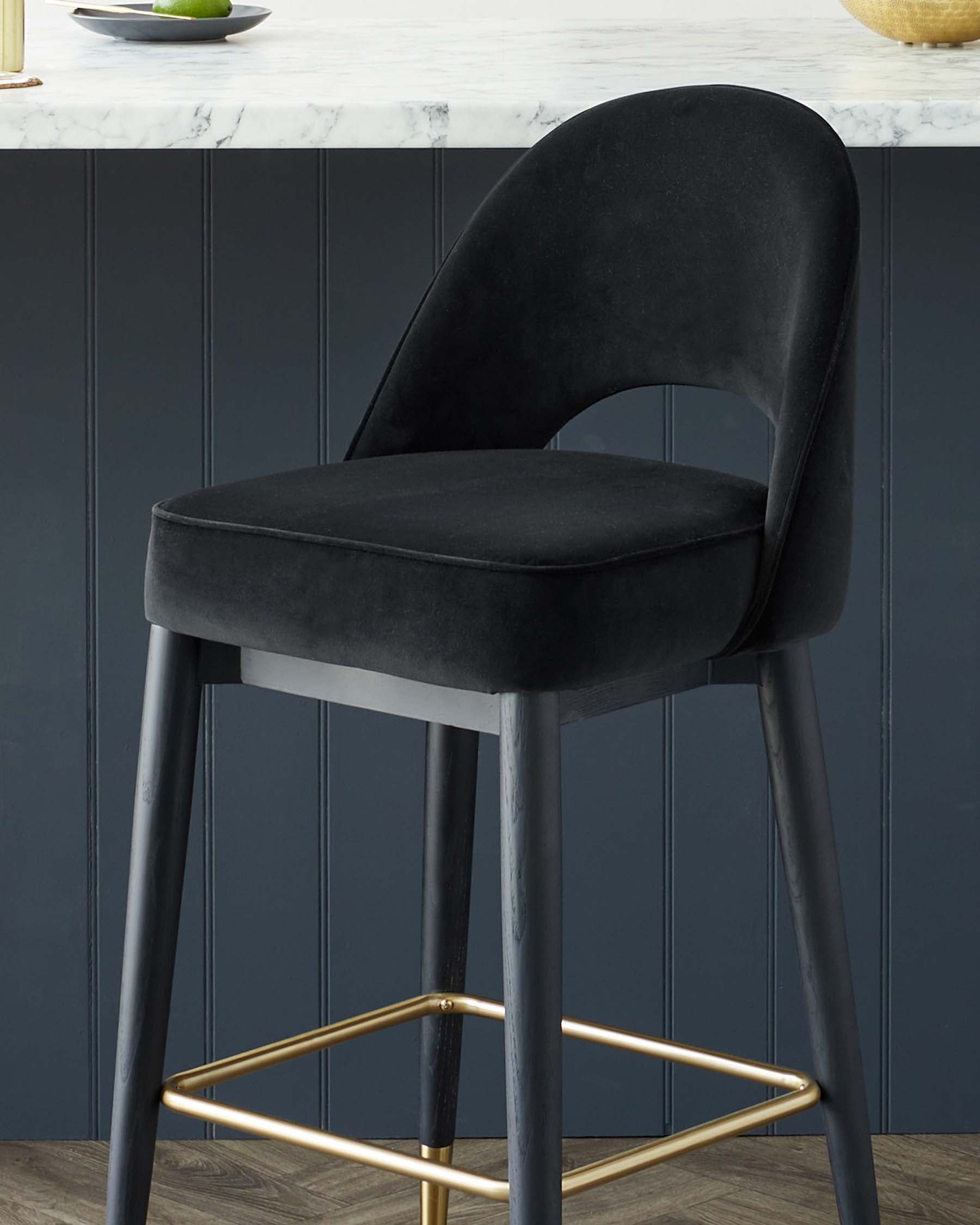 Elegant modern bar stool with a curvaceous black velvet upholstered seat and backrest, featuring sleek black legs with gold-finished footrests.