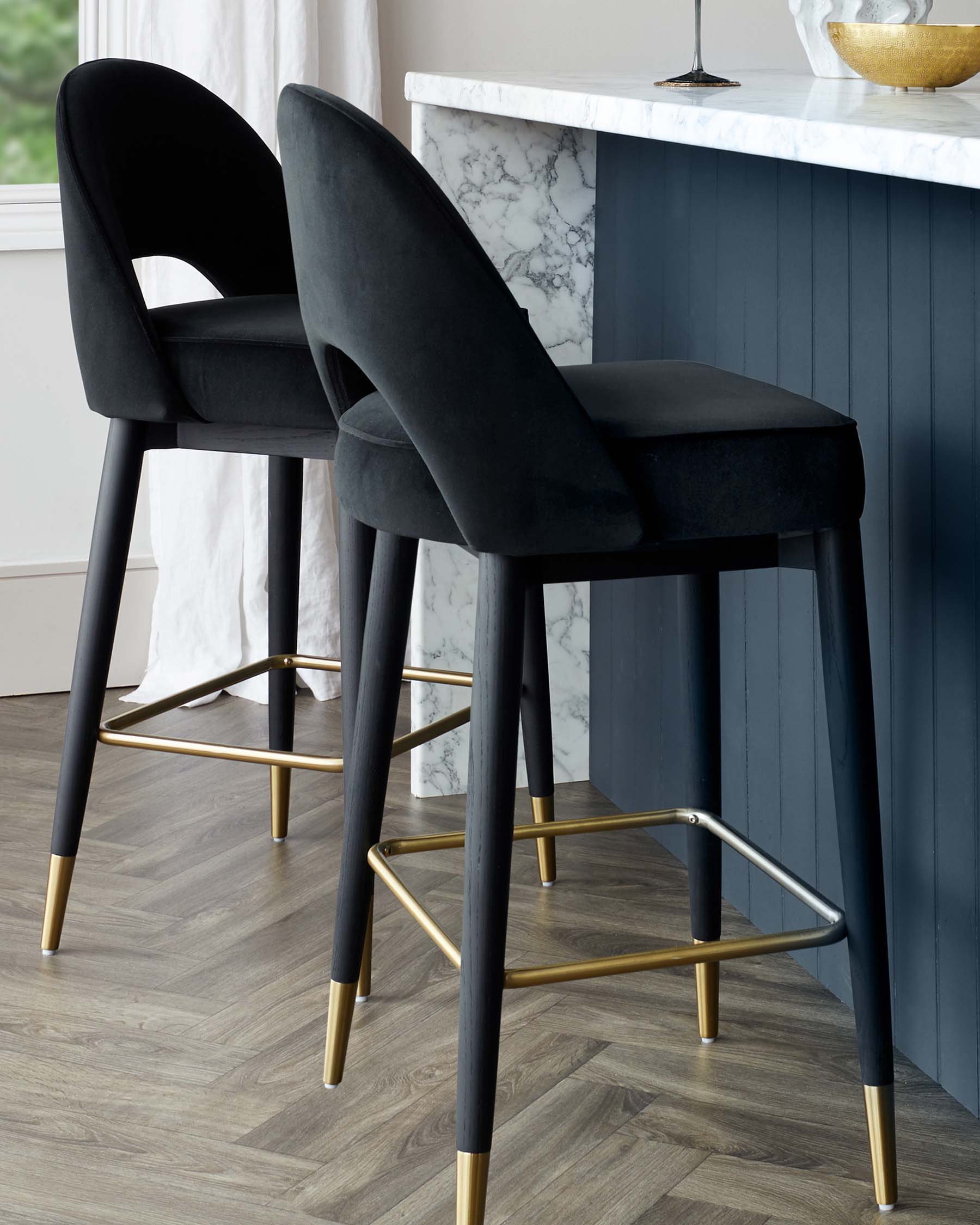 Elegant modern bar stools with plush black velvet upholstery and matte black legs accented with gold tips and footrests.