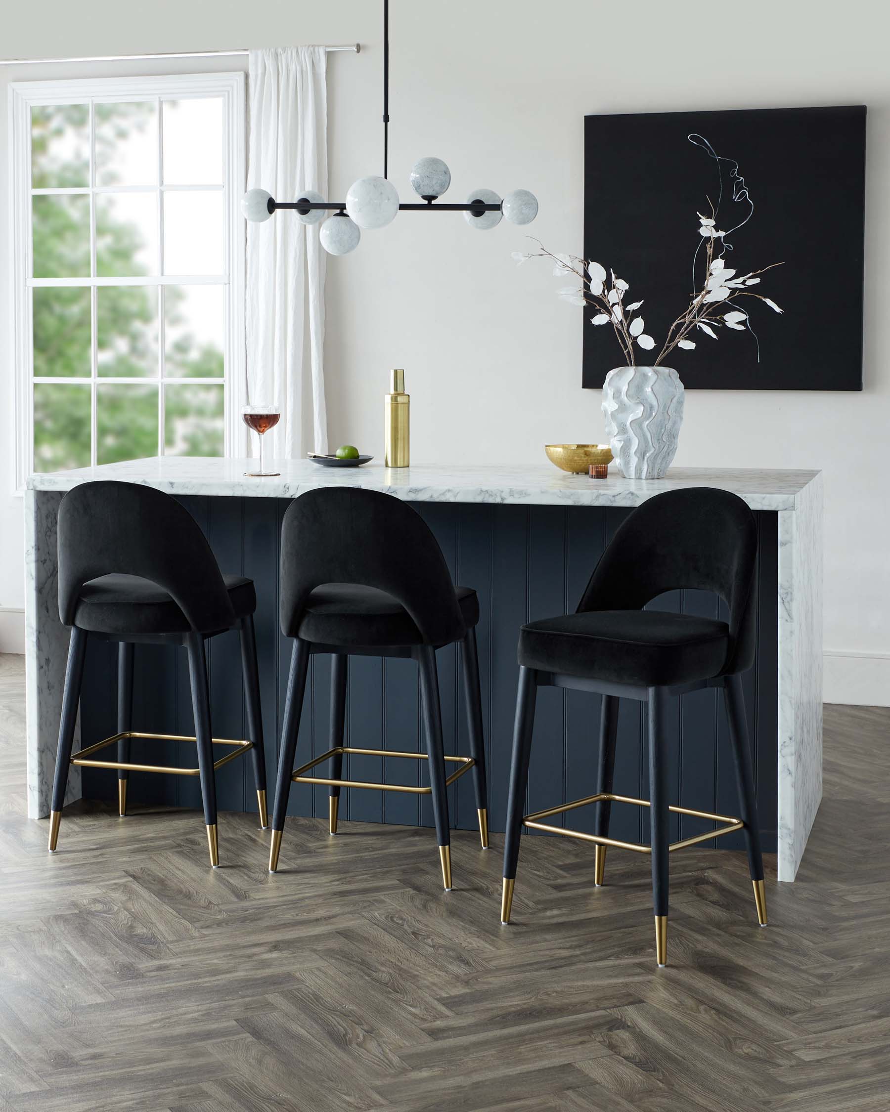 Three elegant black velvet bar stools with sleek brass-finished metal legs arranged at a white marble-topped kitchen island with a navy blue base in a light-filled room.