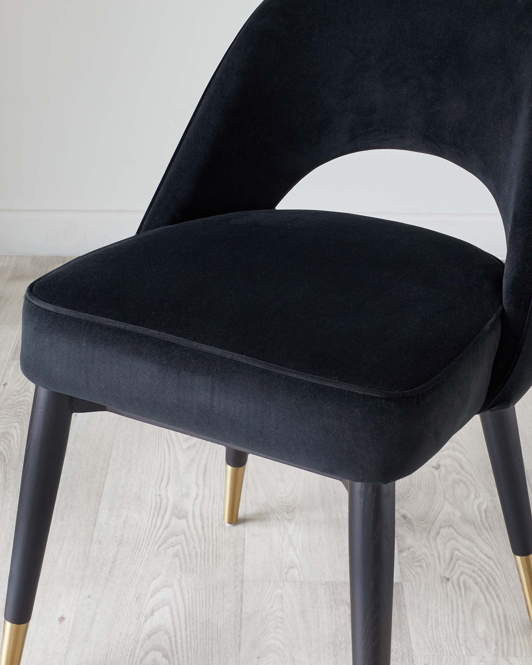 Elegant modern dining chair with plush black velvet upholstery and a smoothly curved backrest. The chair features tapered wooden legs in a dark finish with gold-coloured tips, creating a chic and sophisticated look.