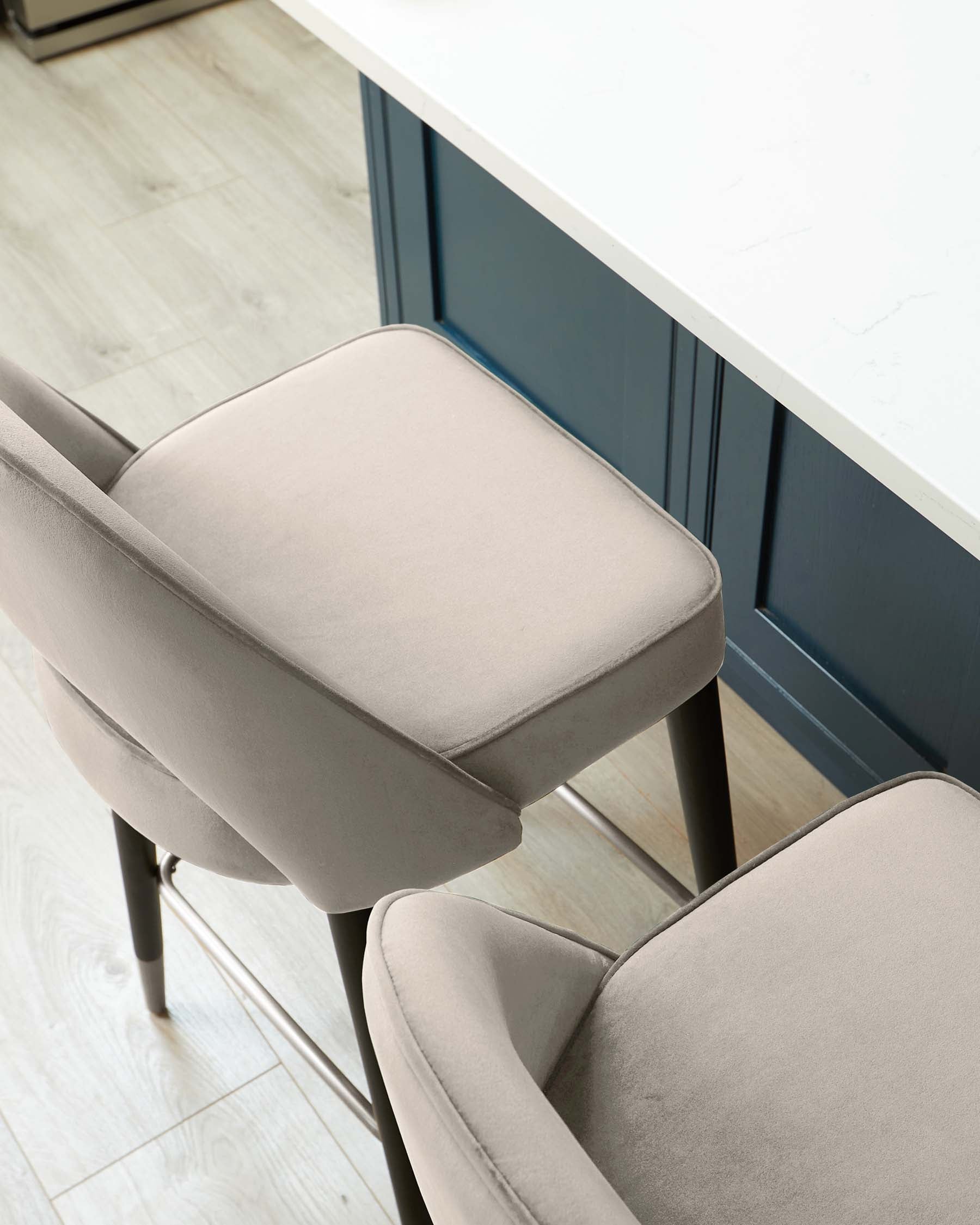 Modern minimalist dining chair with beige fabric upholstery and black metal legs, paired with a white countertop and blue cabinets in a contemporary kitchen setting.