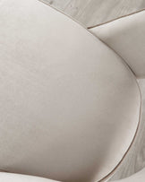 Close-up of a modern chair with a curved backrest and a smooth, light beige upholstery. The fabric appears soft and is neatly tailored with subtle seam details, showcasing the chair's elegant and minimalistic design.