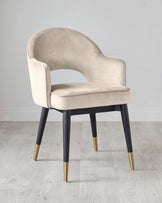 Elegant modern accent chair with a curved backrest and plush light beige velvet upholstery. It features dark wooden tapered legs with stylish gold-coloured tips, creating a chic contrast. Perfect for adding a luxurious touch to any room decor.