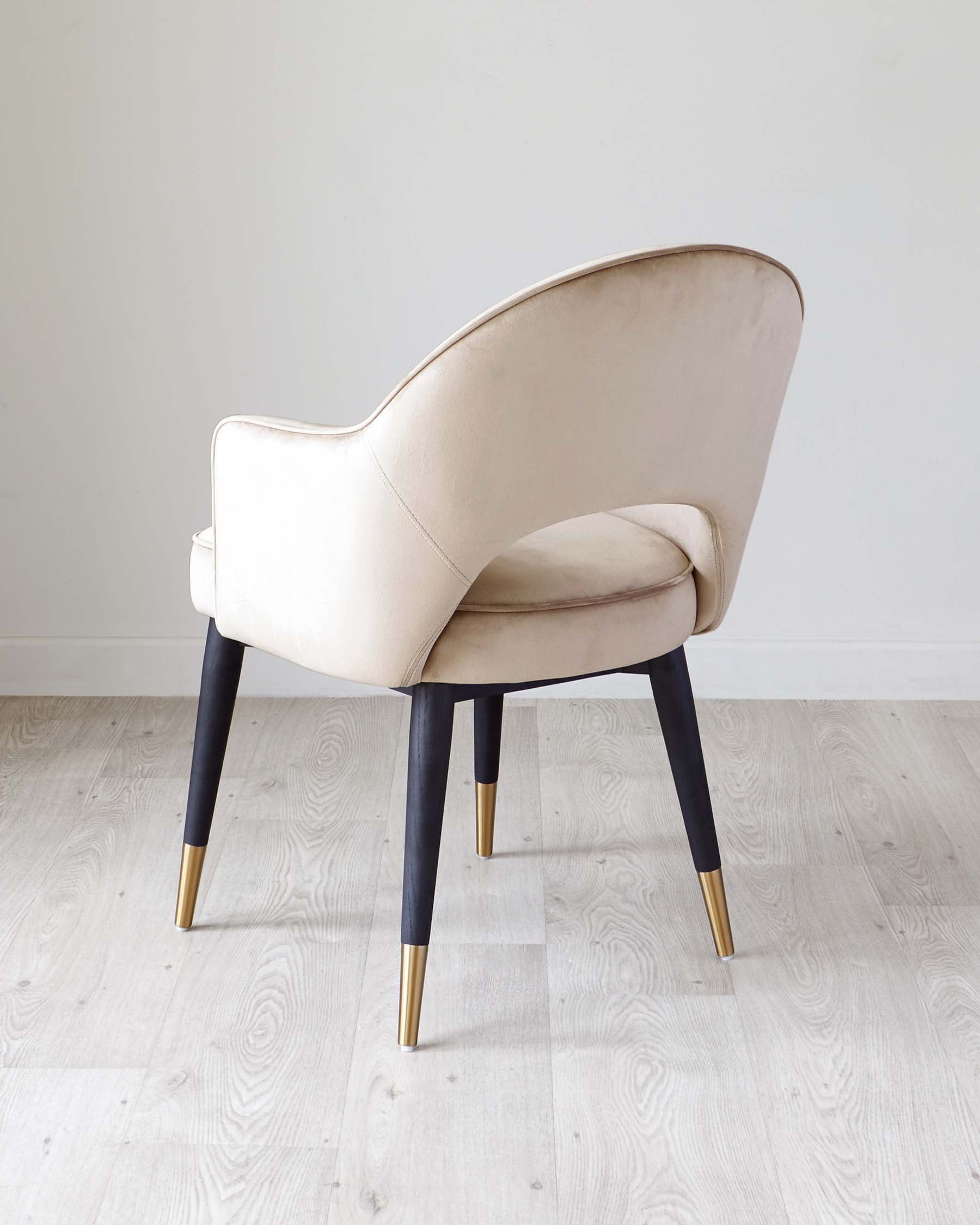 Elegant modern armchair with a curved backrest and cream upholstery, featuring black tapered legs accented with metallic gold tips, set against a neutral background with light wooden flooring.