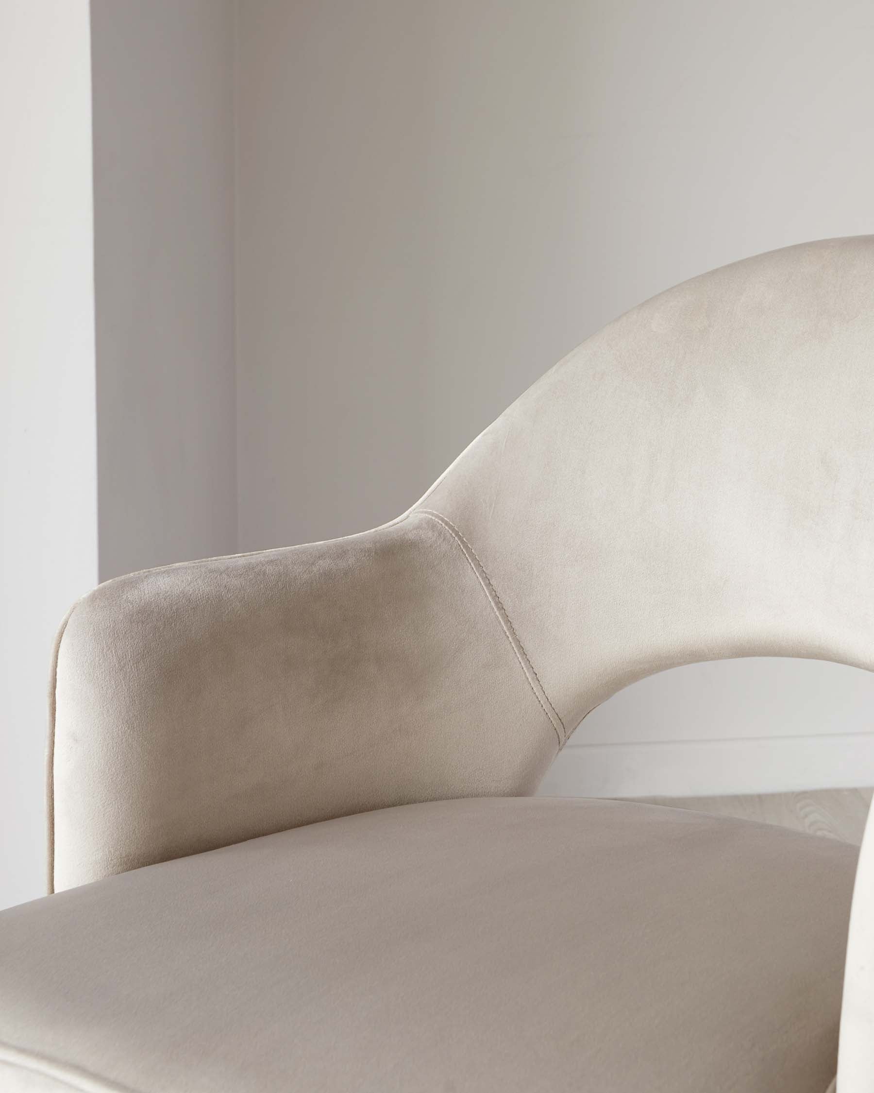 Close-up of a beige upholstered modern chair with a smooth curved backrest and a plush seat, set against a neutral background.