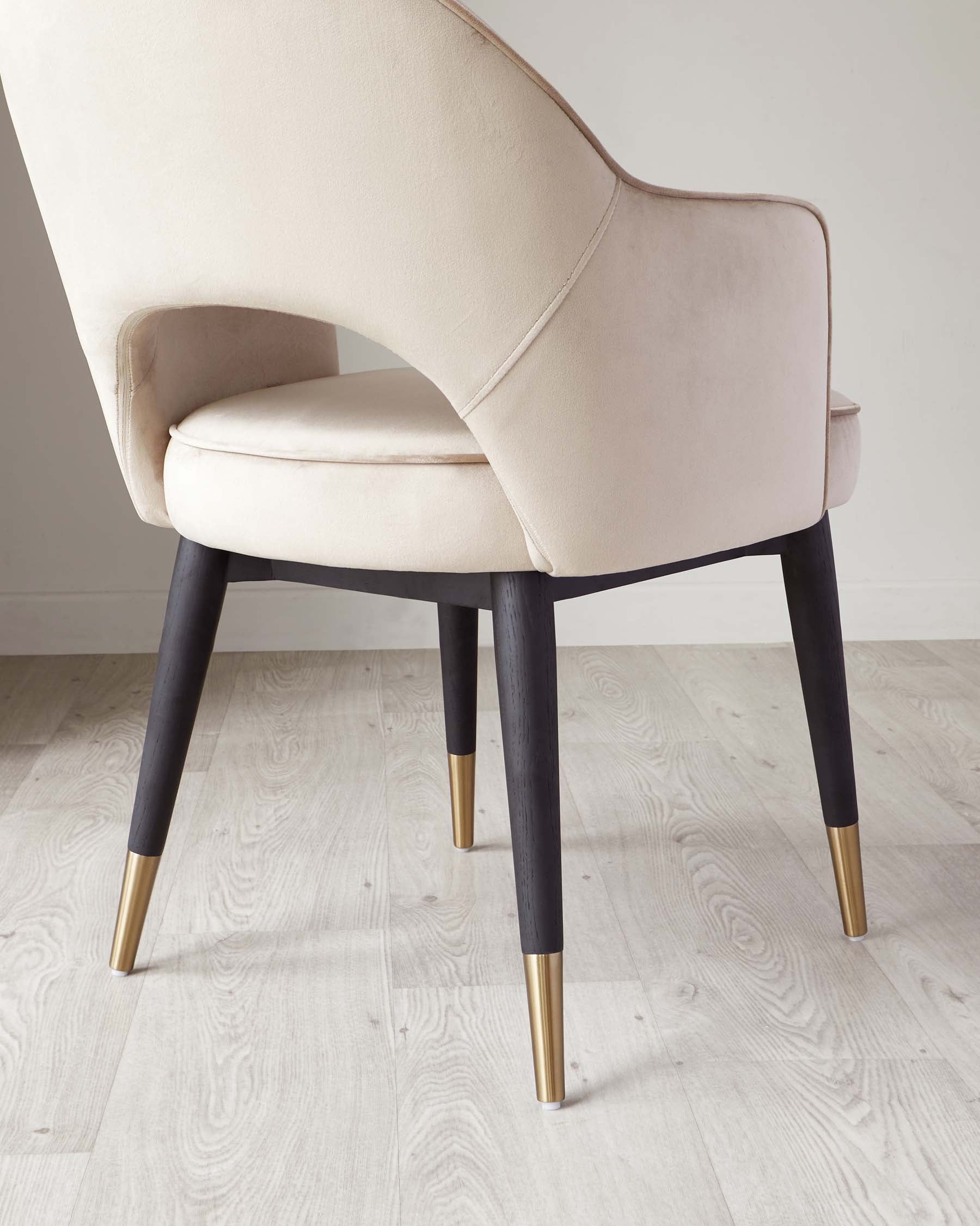 Elegant modern chair featuring a cream upholstered seat and backrest with a smooth curved design and visible seam detailing. The chair stands on four angled solid legs in a dark finish, accented with gold-toned metal tips at the bottom, set against a light wood floor.