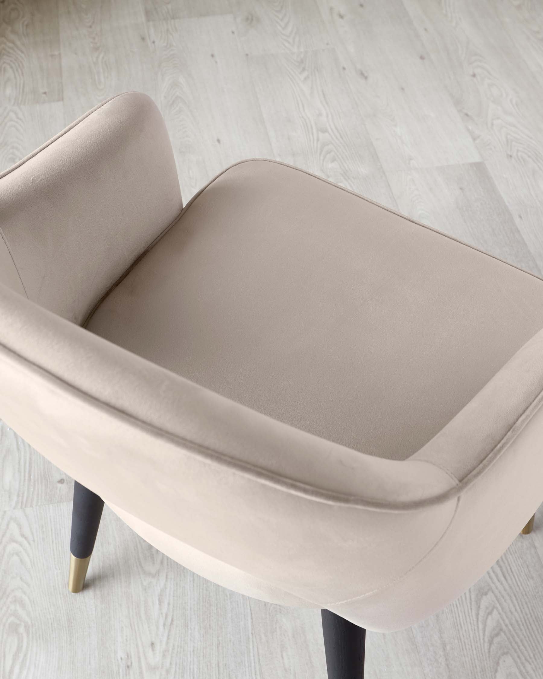 Elegant contemporary chair with a minimalist design, featuring a smooth, light beige upholstery and dark, tapered legs with golden feet caps, set against a light wooden floor.