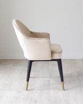 Elegant modern chair with beige upholstery and contrasting black legs with gold tips.