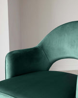 Elegant dark green velvet accent chair with a smoothly curved backrest and a plush seat, set against a neutral background.