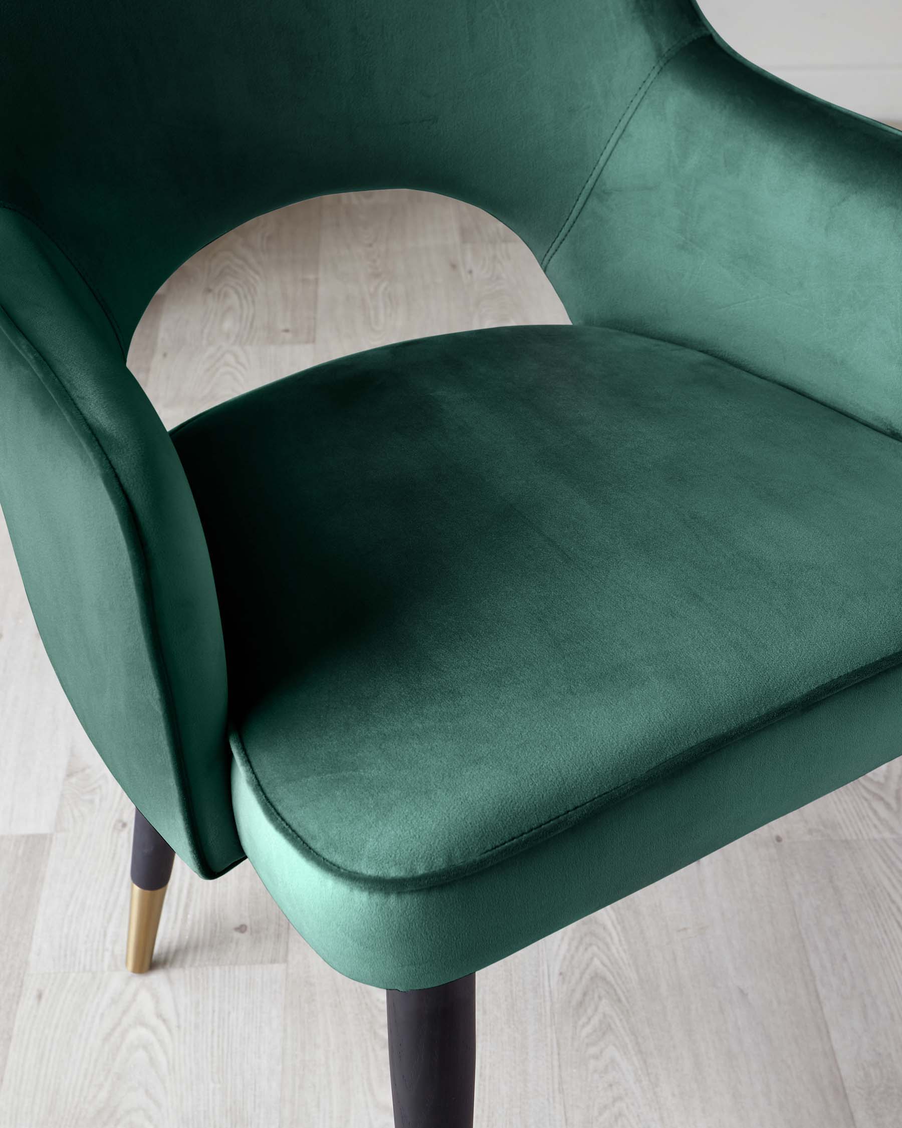 Elegant modern armchair with plush emerald green velvet upholstery, featuring a curved backrest and a comfortable, thick seat cushion. The chair is supported by tapered wooden legs with a dark finish and contrasting gold-capped feet.