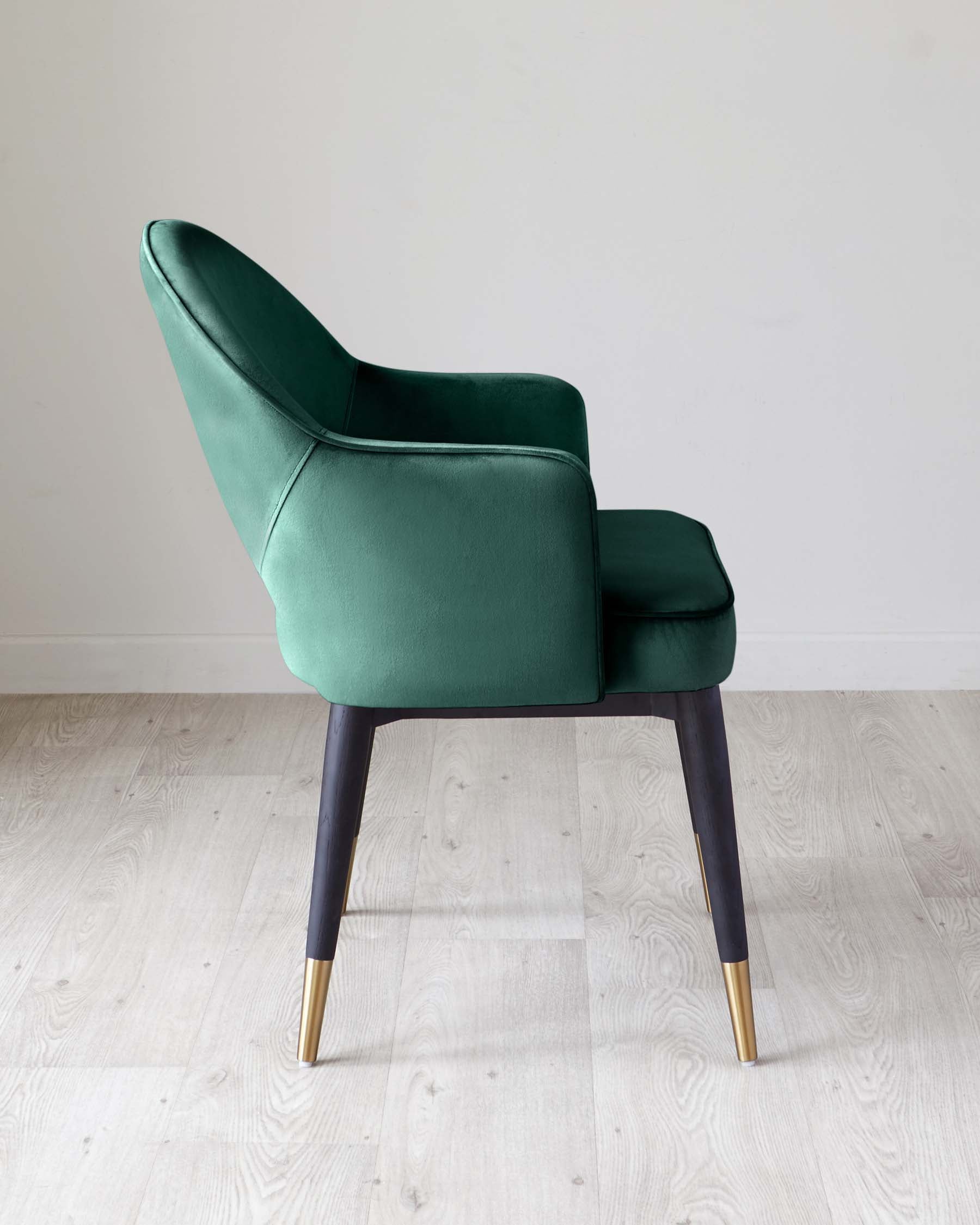 Elegant emerald green upholstered armchair with a high backrest and a matching ottoman. The chair has dark wooden legs tipped with brass accents, set against a neutral background and light wooden flooring.