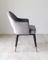 Elegant modern accent chair with a high curved backrest, upholstered in a smooth grey fabric, featuring sleek black wooden legs tipped with stylish gold accents, displayed against a neutral backdrop.