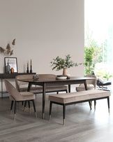 Elegant modern dining room set featuring a dark wood oval table with sleek tapered legs tipped with brass accents. Includes two plush, upholstered armchairs with matching wooden legs and brass details, and a coordinating bench with similar design attributes. The set conveys a sense of contemporary sophistication suitable for a stylish dining space.