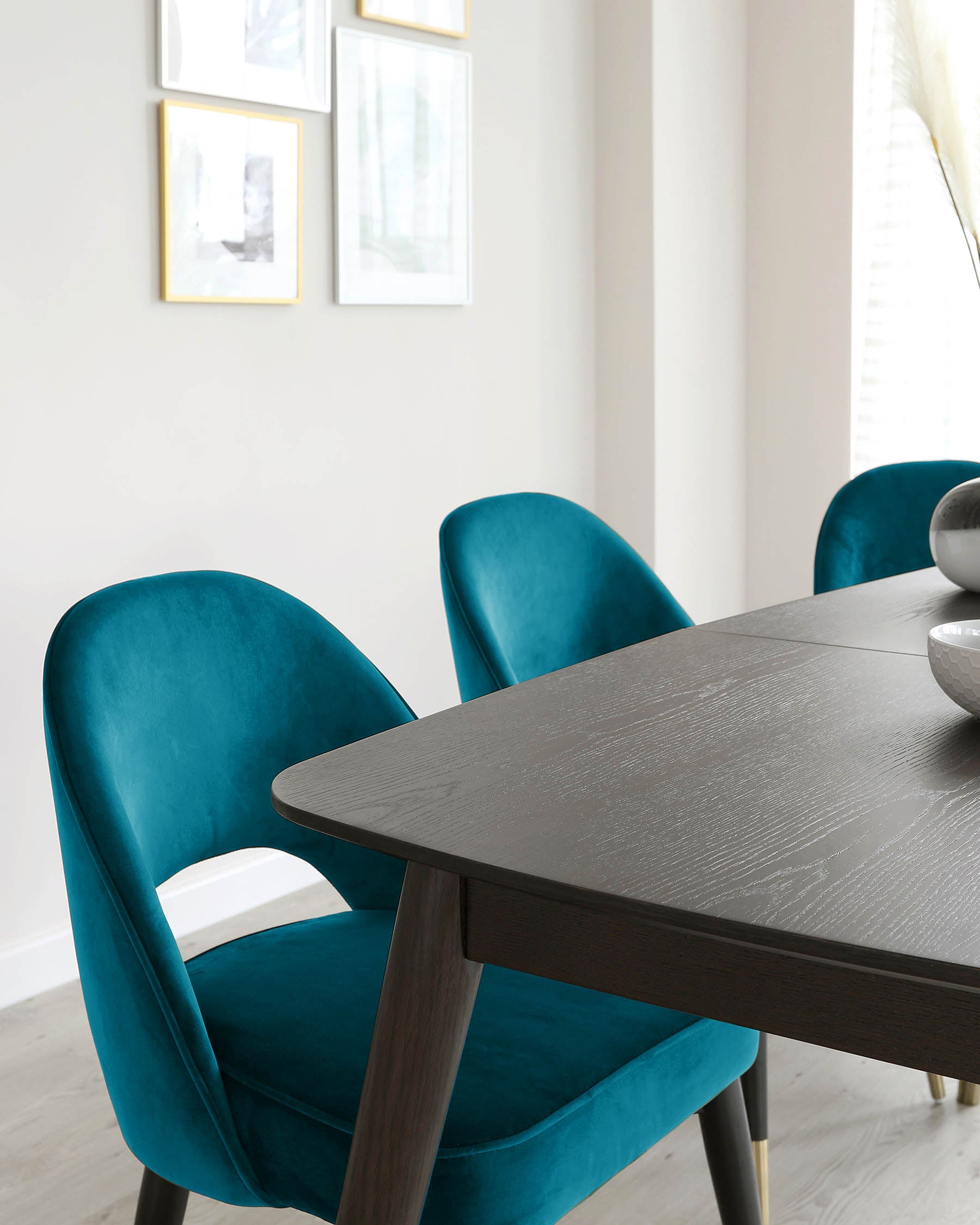 Elegant dining room furniture featuring a dark wood table with a textured finish and angled legs, accompanied by plush teal blue velvet dining chairs with a curved backrest and sleek black legs.