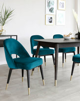 Modern dining room furniture consisting of a dark wood table with tapered legs and plush teal velvet upholstered chairs with a gold-tipped leg design.