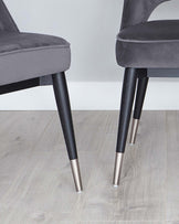 Elegant modern dining chairs with soft grey velvet upholstery and contrasting dark wooden legs capped with silver metal tips.