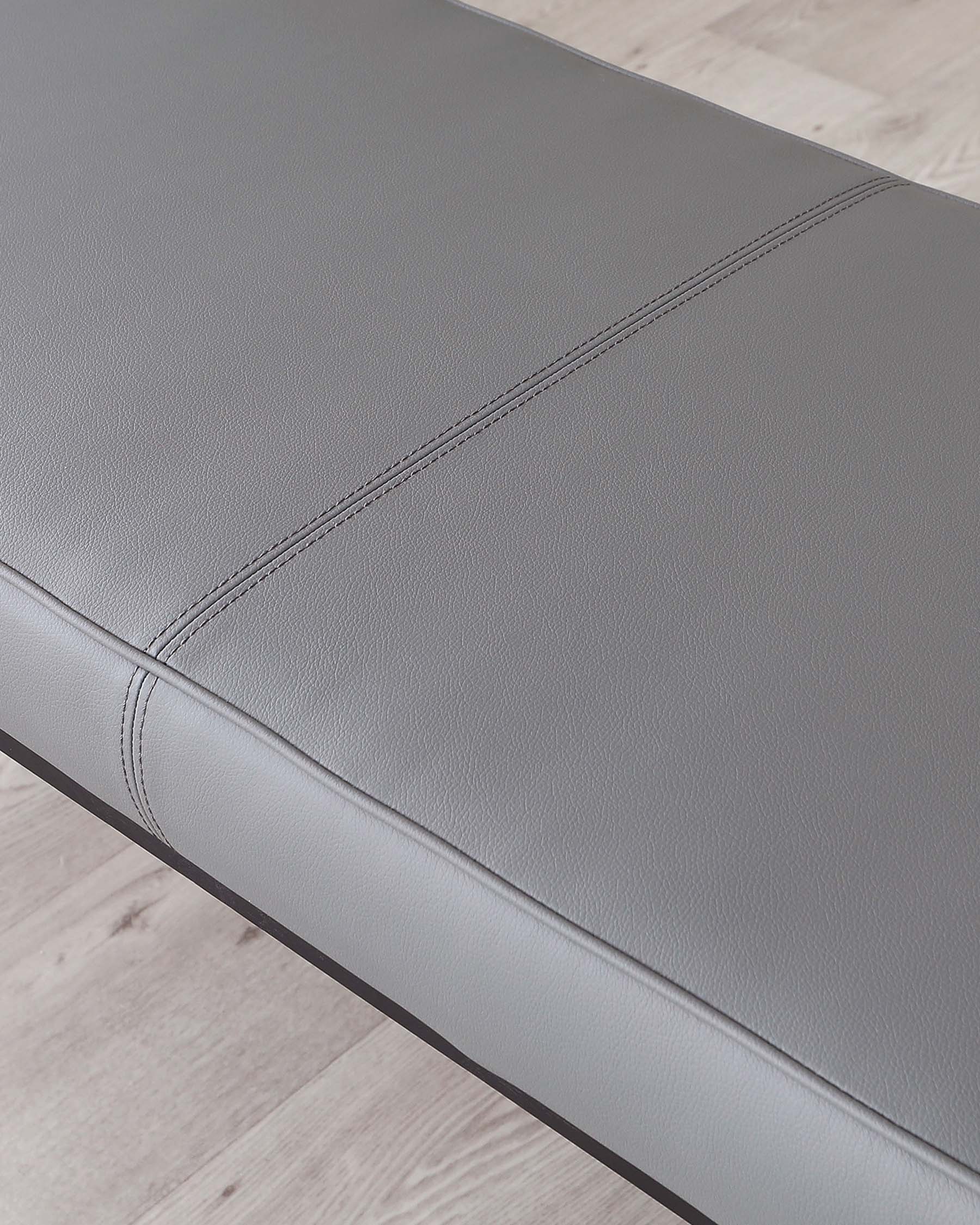 Modern grey upholstered bench with fine stitch detailing and sleek black legs, depicted on a light wooden floor.