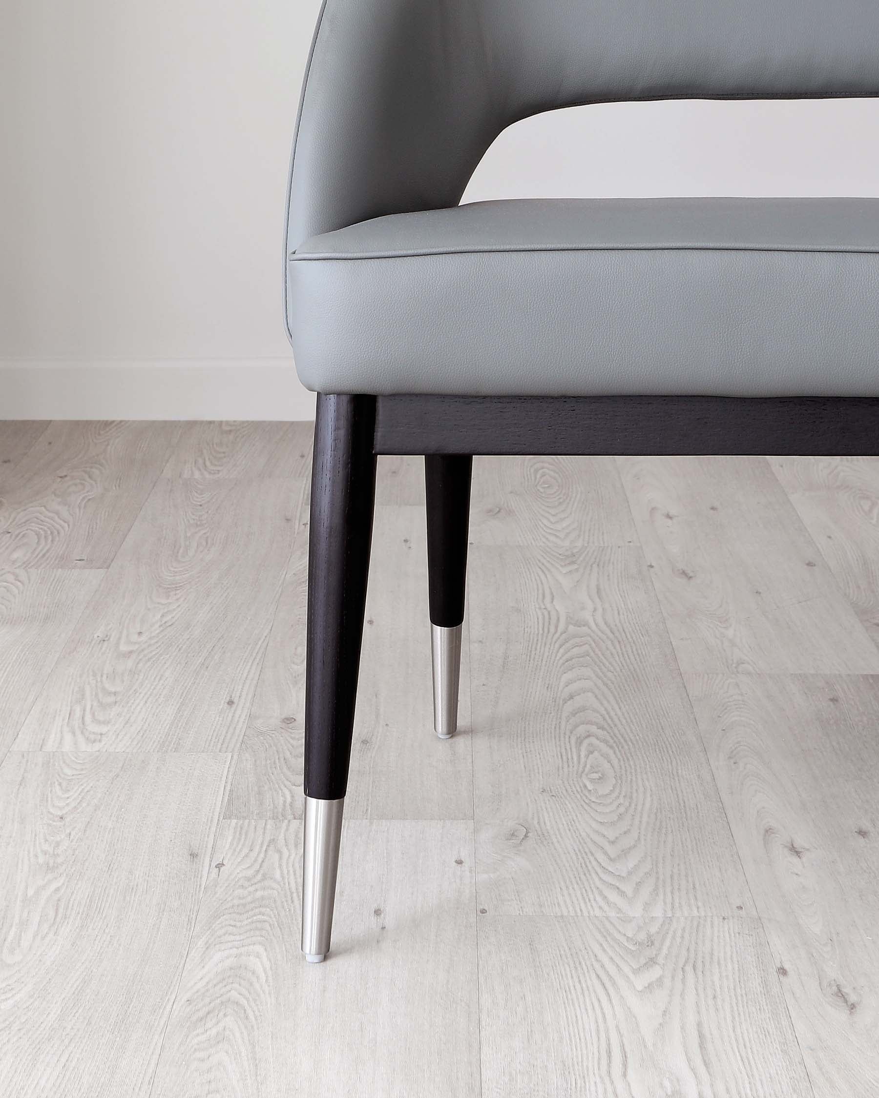 Contemporary armchair with light grey upholstery and dark wooden legs featuring metallic silver tips, set against a light wooden floor and off-white wall.