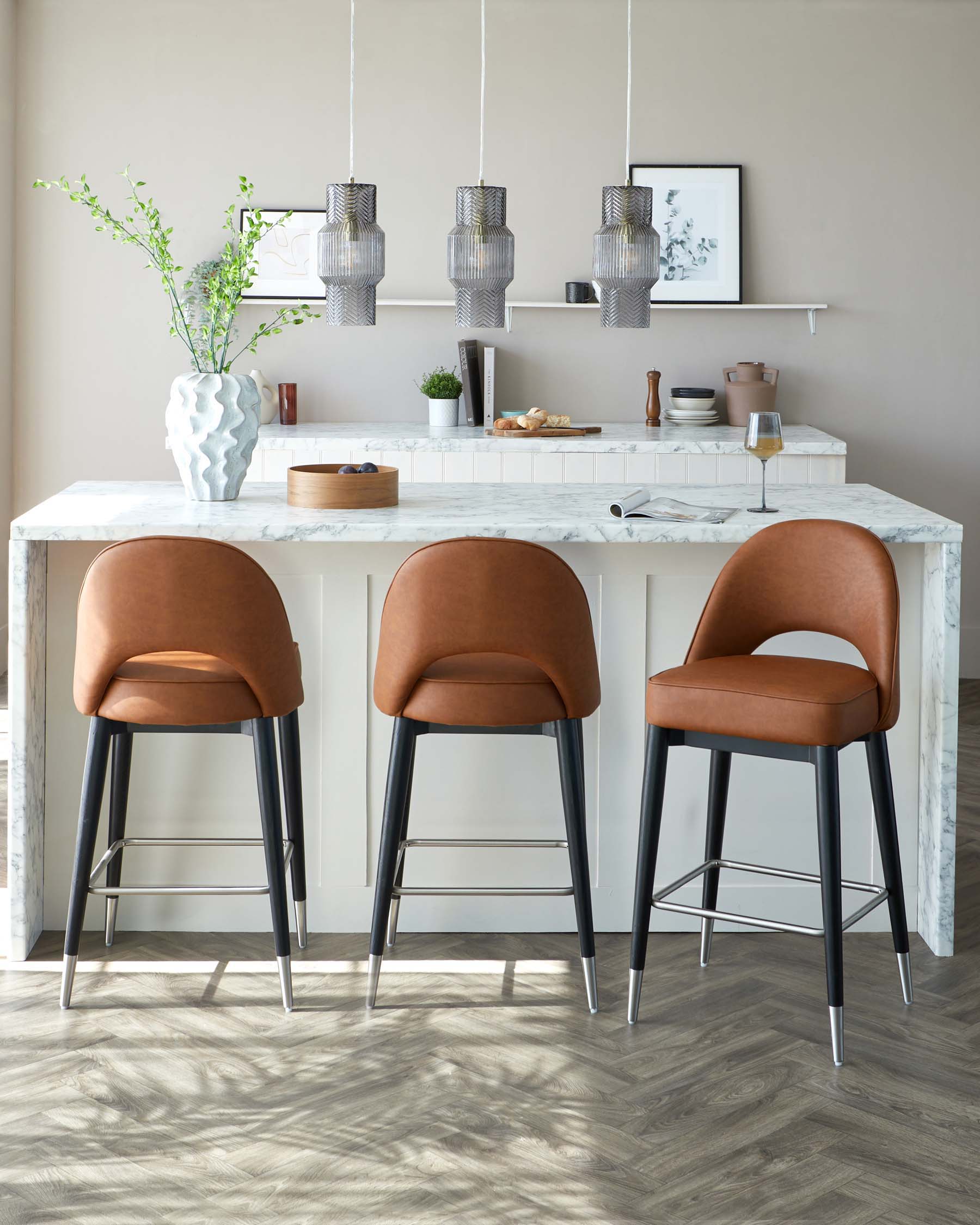 Modern kitchen interior featuring three caramel brown leather upholstered bar stools with black metal legs, nestled against a white marble countertop kitchen island.