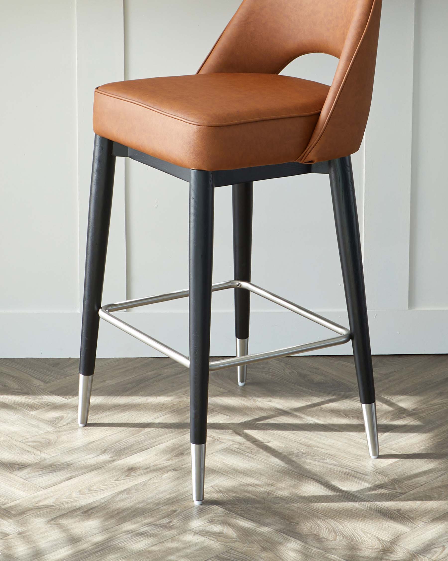 Elegant contemporary bar stool featuring a warm caramel faux leather seat with a curved mid-back design, and sturdy black metal legs accented with sleek silver tips and a geometric footrest in a contrasting chrome finish.