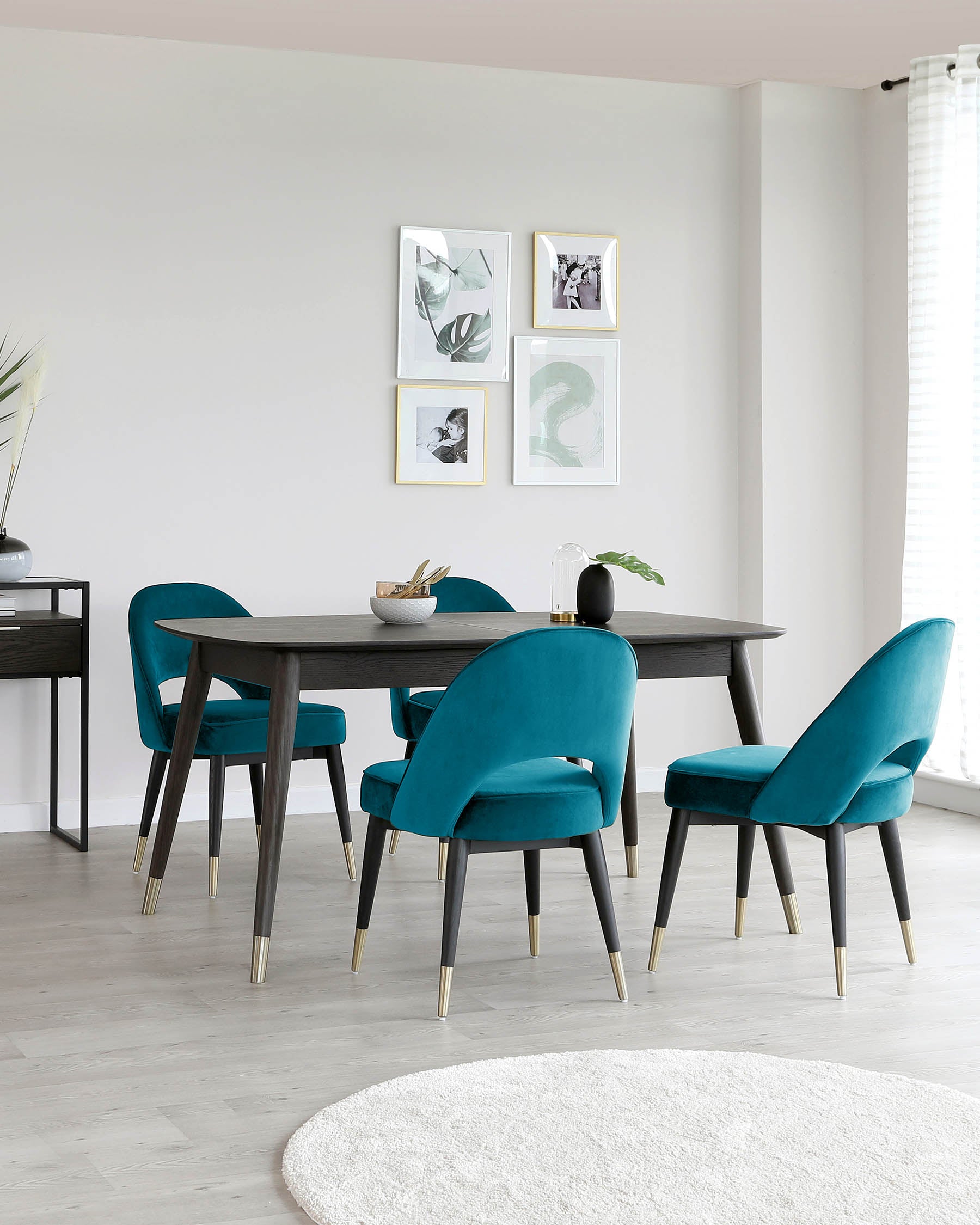 Contemporary dining room furniture featuring a rectangular, dark wood table with sleek lines and four teal upholstered chairs with black legs tipped with gold accents. A matching dark wood console table is visible in the background.