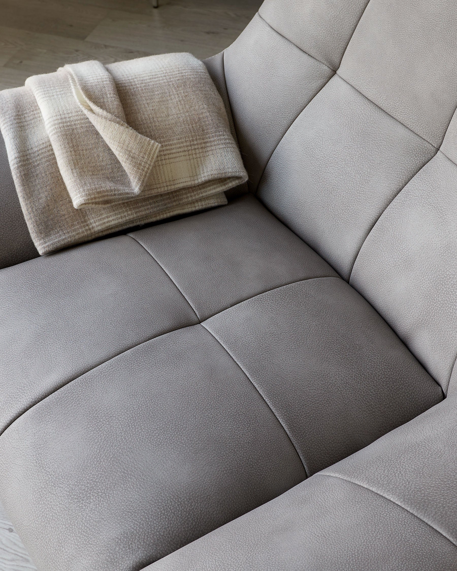 Close-up of a contemporary light grey leather armchair with a plush design featuring tufted cushions and a soft beige checkered throw blanket neatly folded on one armrest.