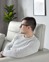 Modern light grey leather sofa with a high backrest and cushioned armrests in a contemporary living room setting, complemented by a minimalist framed artwork and a verdant potted plant in the background.