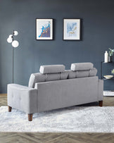 A modern L-shaped sectional sofa in a light grey fabric with three cushions along the back and a chaise on the left side. The sofa has simple, clean lines with unadorned arms and is supported by tapered wooden legs in a dark finish. It rests on a white and grey patterned area rug that adds texture to the space. A sleek black sideboard with decor items is partially visible in the background to the right.