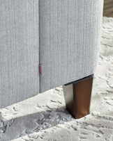 Close-up of a modern sofa leg, showcasing a sleek metal design with a reflective finish, complemented by soft heathered upholstery fabric in a neutral grey tone.