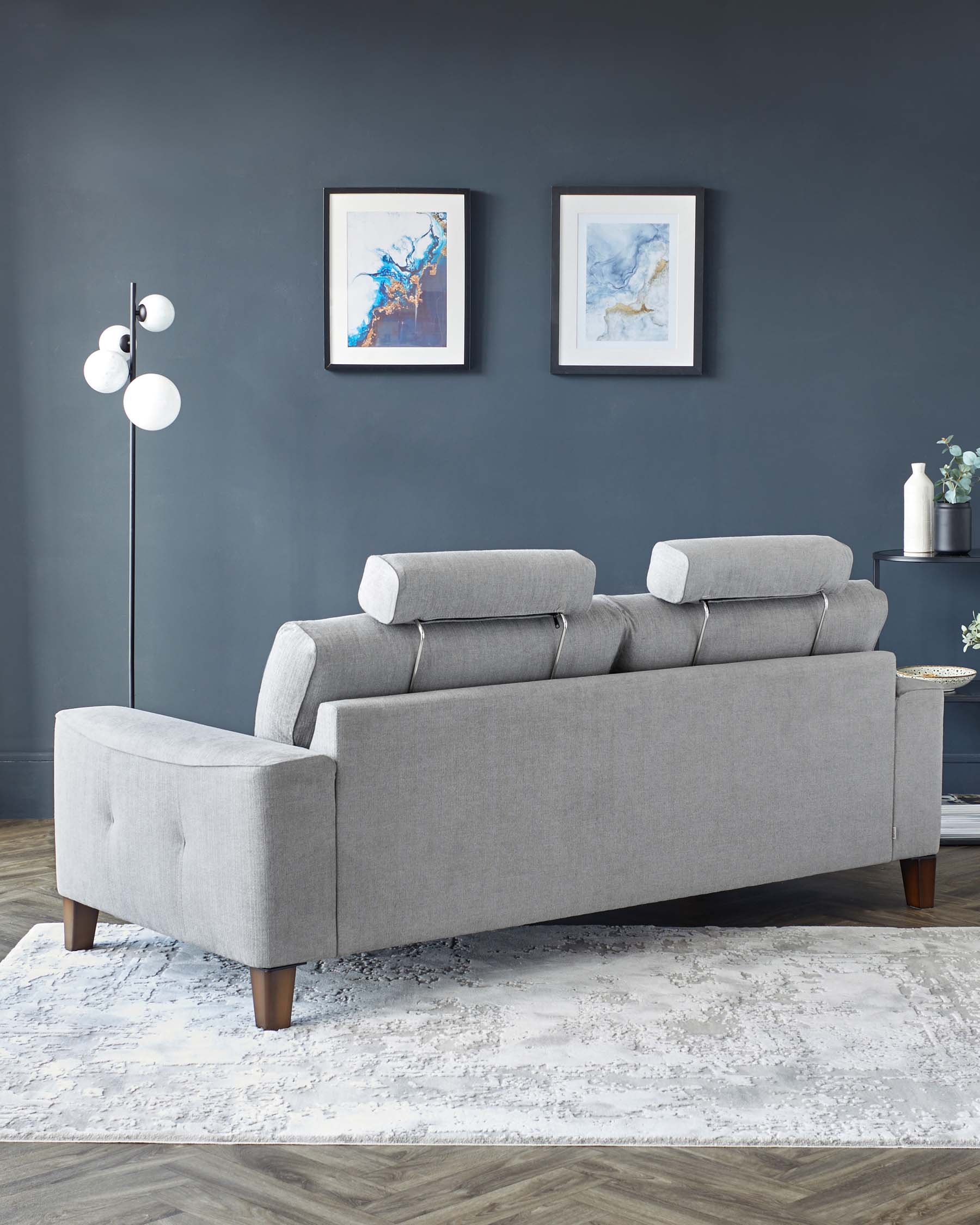 Modern grey fabric sectional sofa with cylindrical cushions, wooden legs, and a chaise lounge extension on a textured white and grey area rug.