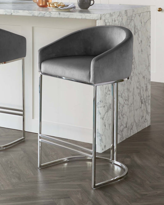 Elegant modern bar stool with a curved backrest, upholstered in a plush grey velvet fabric, complemented by a sleek chrome-finished metal frame with an integrated footrest.