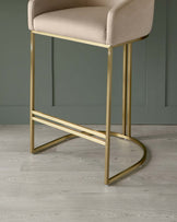 Elegant modern bar stool featuring a soft beige upholstered seat and backrest, with a sleek golden metal frame providing both support and a chic accent. The design includes a minimalist high back and a curved footrest for comfort.