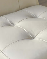 Close-up of a cream-colored leather upholstery with deep button-tufted detailing, showcasing the fine texture and elegant design suitable for luxurious seating furniture.