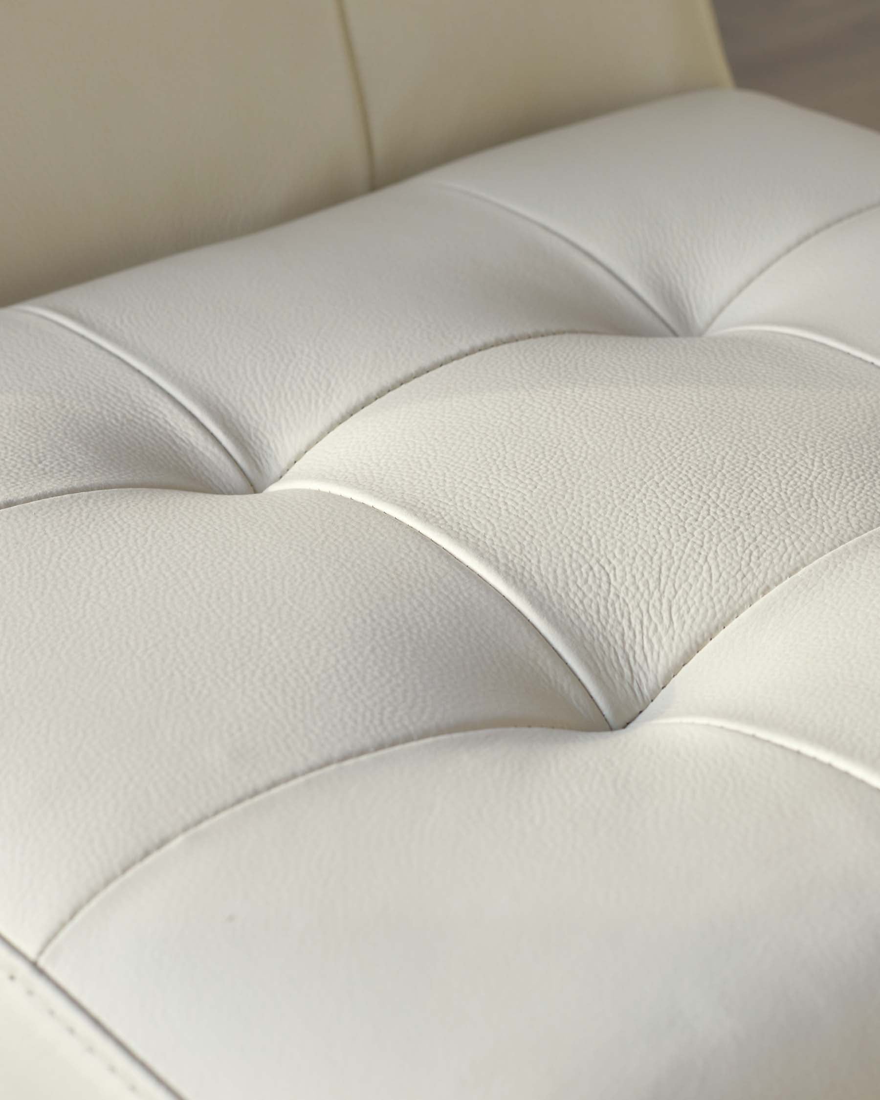 Close-up of a cream-colored leather upholstery with deep button-tufted detailing, showcasing the fine texture and elegant design suitable for luxurious seating furniture.