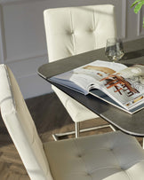 Modern dining area featuring a sleek dark stone tabletop with distinctive grain patterns and two cream-colored, tufted, upholstered dining chairs with a contemporary design and clean lines, complemented by elegant steel chair frames. A design magazine lies open on the table beside a clear, stemless glass, subtly suggesting a relaxed yet sophisticated lifestyle.