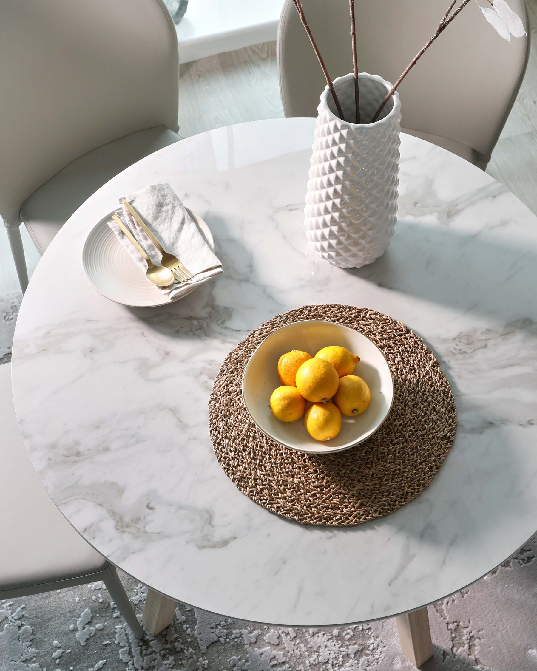 Elegant round marble-top dining table with natural wood tapered legs, accompanied by modern curved-back chairs in a soft matte finish.